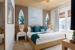A bedroom with a bed, bedside tables, a nightstand, a window with curtains, and a wall with vertical slats and a mural.
