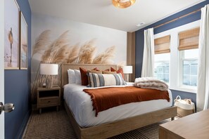 A bedroom with a bed, bedside tables, a nightstand, a window with curtains, and a wall with a decorative wall art piece.