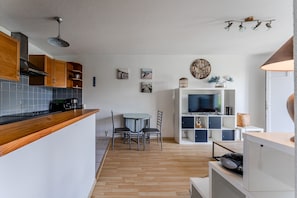 A modern kitchen with wooden cabinets, a dining table, and chairs. There is a TV and a bookshelf in the living area. - Bel Air with Private Terrace and Garden, 10-Min Walk to Market (La Teste-de-Buch)