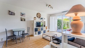 A modern living room with a TV, wooden flooring, a dining area with chairs, a sofa, and a lamp. - Bel Air with Private Terrace and Garden, 10-Min Walk to Market (La Teste-de-Buch)