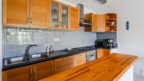 A modern kitchen with wooden cabinets, a black countertop, stainless steel appliances, and a wooden island. - Bel Air with Private Terrace and Garden, 10-Min Walk to Market (La Teste-de-Buch)