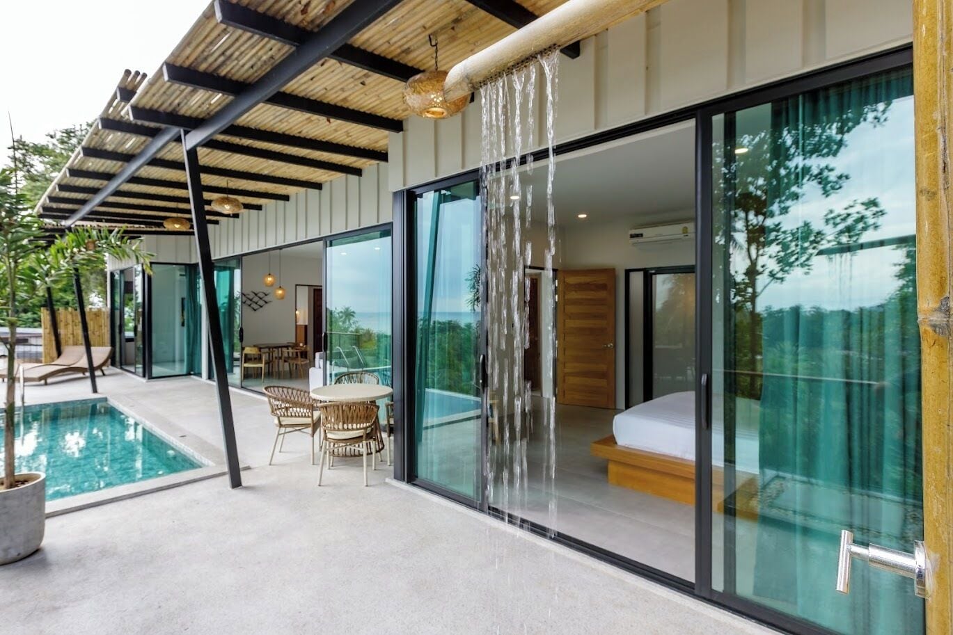 Een modern huis met een slaapkamer met glazen wanden, een zwembad en tuinmeubilair.