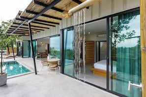 Une maison moderne dotée d’une chambre à coucher entièrement vitrée, d’une piscine et de mobilier d’extérieur.