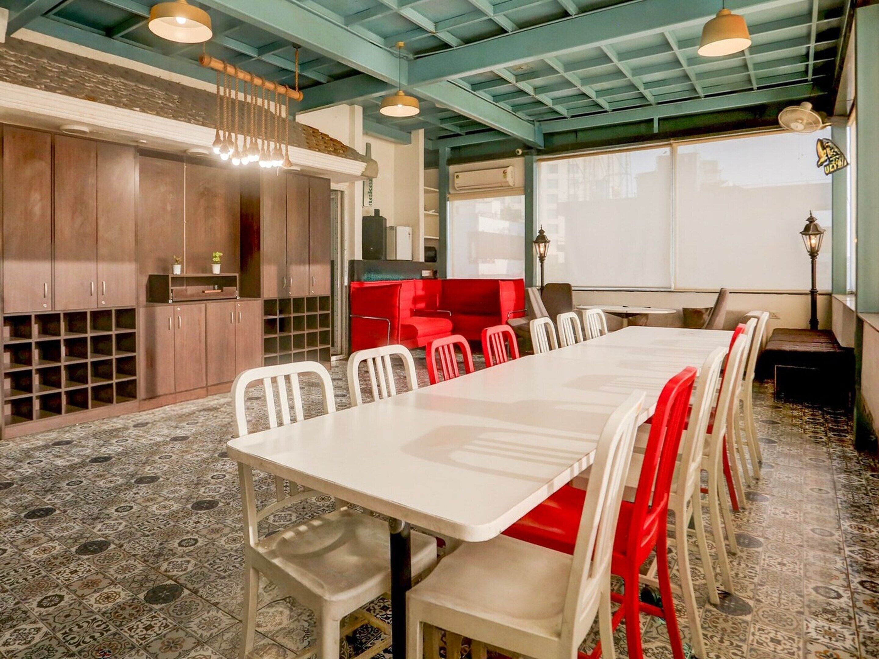 A dining area with a long table, chairs, and a red booth. There are cabinets and a ceiling with exposed beams.