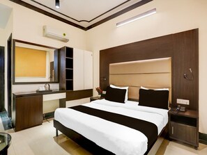 A hotel room with a large bed, a bedside table with a phone, a mirror, a wardrobe, and a built-in air conditioning unit. - Townhouse Sushant Lok Phase 1 Hotel Neven (Gurugram)