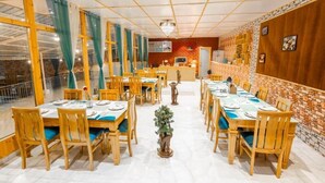 A restaurant with wooden tables and chairs, a central plant, and a brick wall. - We are one paradise (Mussoorie)