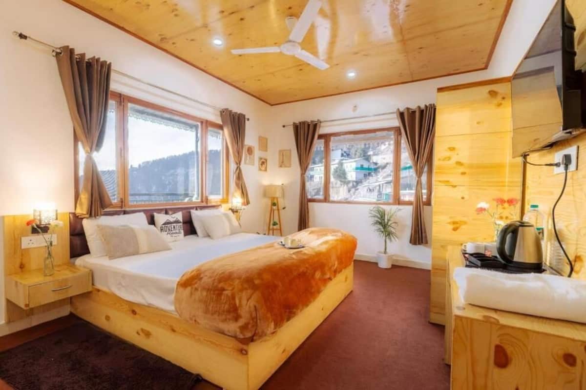 Un dormitorio de madera con cama, mesitas de noche, ventilador de techo y ventanas amplias.