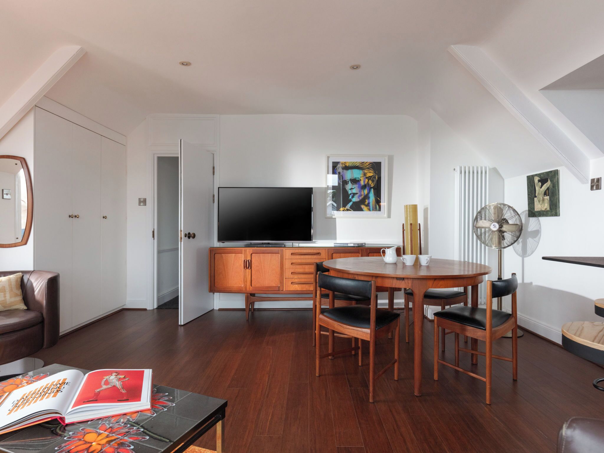 Un salon moderne avec un téléviseur à écran plat, des meubles en bois, une table à manger et un livre posé sur une table basse.
