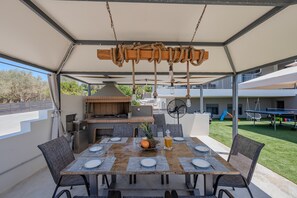 Ein Essbereich im Freien mit einem Tisch für vier Personen, einem Grill und einem Ventilator.
