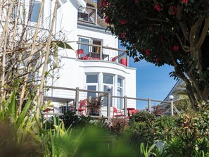 Un bâtiment blanc doté de balcons, d’une façade incurvée et d’un jardin avec des chaises rouges.