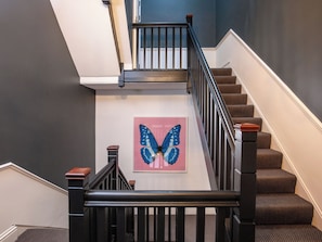 Eine Treppe mit schwarzem Geländer, ein blaues Schmetterlingsbild an der Wand und ein braun ausgelegter Boden.