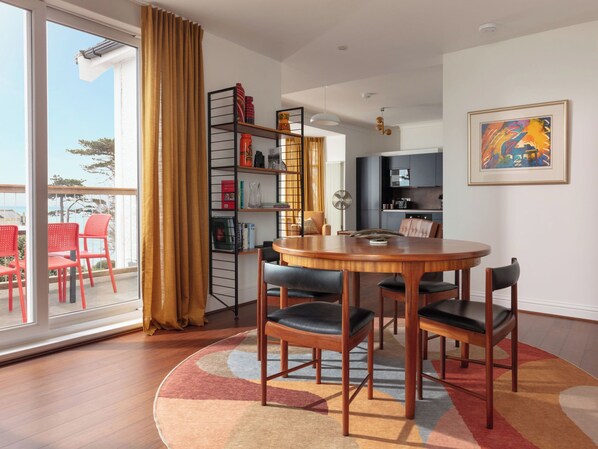 Un espace repas moderne avec une table ronde en bois, des chaises noires et une bibliothèque contenant divers objets.