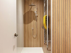 Une salle de bain avec un mur recouvert de panneaux en bois, une douche et un porte-serviettes sur lequel est posée une serviette jaune.