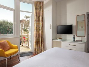 Une chambre d’hôtel équipée d’un lit, d’une télévision, d’un bureau avec un ordinateur, d’une chaise et d’une fenêtre avec des rideaux.