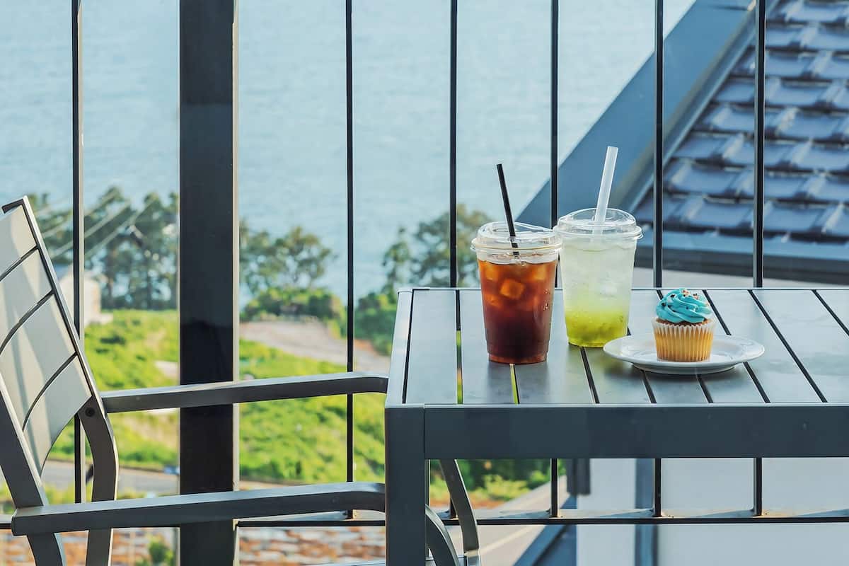 Un balcón con una mesa lista para dos personas, con dos bebidas y un cupcake.