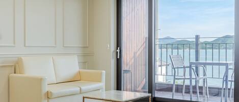 A modern living room with a white sofa, a small table, and a sliding glass door leading to a balcony with chairs.