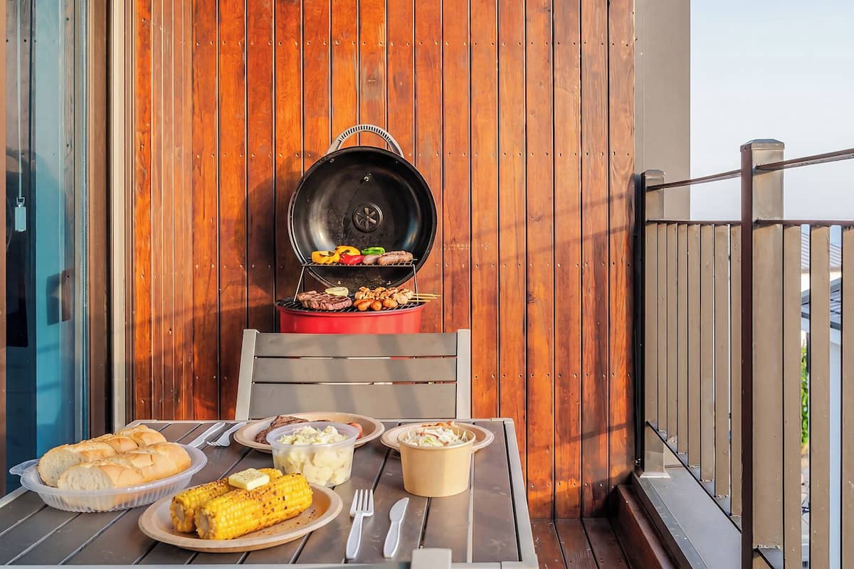 Un balcón con una parrilla, mesa de madera y alimentos.