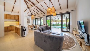 Una cocina moderna con armarios de madera, una zona de comedor con mesa y sillas, un sofá gris y un televisor sobre un mueble de madera.