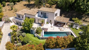 Una casa de dos pisos con piscina, mobiliario exterior y jardín.