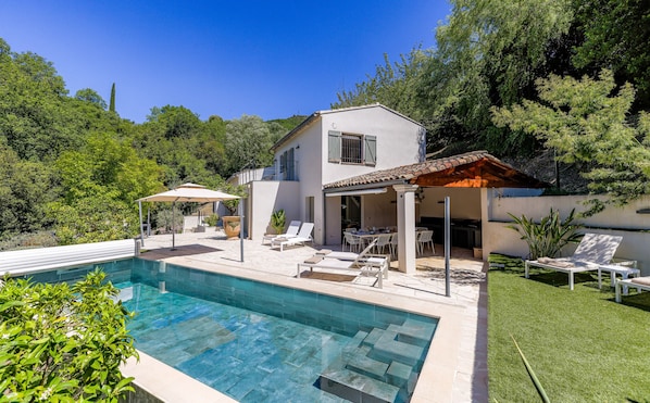 Eine moderne Villa mit Swimmingpool, Sitzgelegenheiten im Freien und einem Garten.