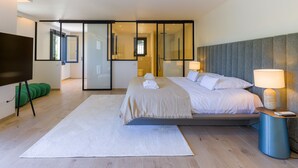 Un dormitorio moderno con cama, lámparas de noche, televisor y un espejo grande.