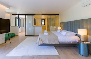 Ein modernes Schlafzimmer mit einem Bett, Nachttischlampen, einem Fernseher und einem großen Spiegel.