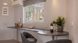 Une cuisine moderne avec une fenêtre, une table à manger, deux chaises, une plante en pot, une bouteille de vin et un saladier de fruits.