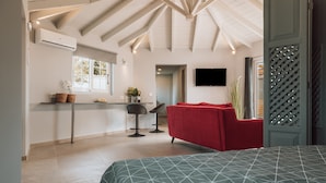 Un intérieur moderne comprenant un lit, un canapé rouge, un coin cuisine et un téléviseur fixé au mur.
