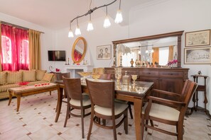 A dining area with a wooden table and chairs, a sofa, and a television on the wall. - Amalia Country House (Zakynthos)