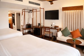 A hotel room with two beds, a desk with a chair, a television, and a sofa with cushions. - Nexus House An Thuong – Boutique Hotel Near My Khe Beach (Da Nang)