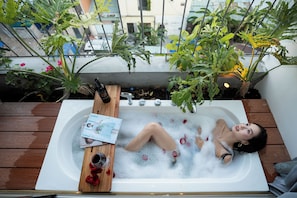 A person relaxing in a bathtub filled with bubbles, with a magazine and a bottle of wine on a wooden tray beside them. - Nexus House An Thuong – Boutique Hotel Near My Khe Beach (Da Nang)