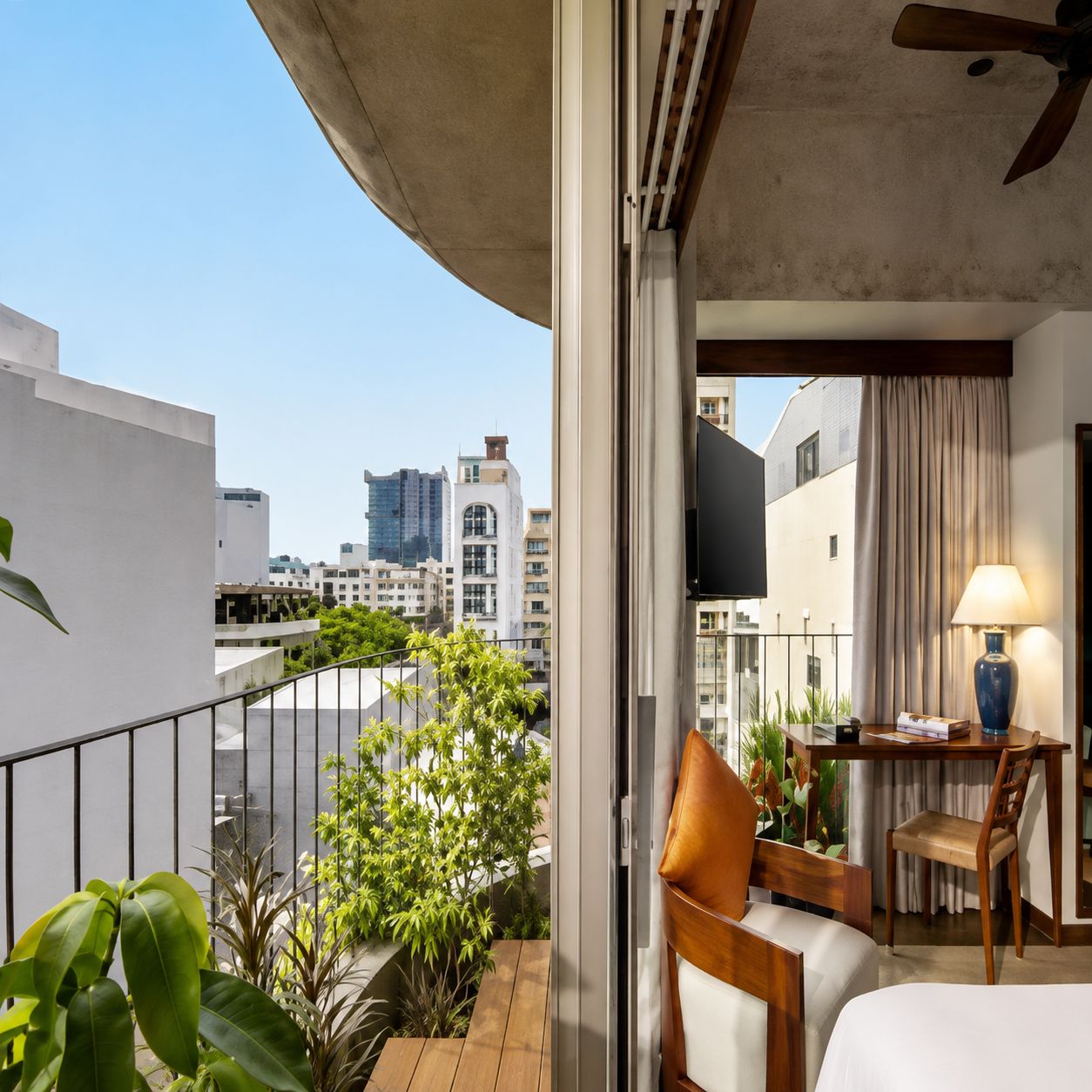 A hotel room with a balcony, a bed, a desk with a chair, and a TV.