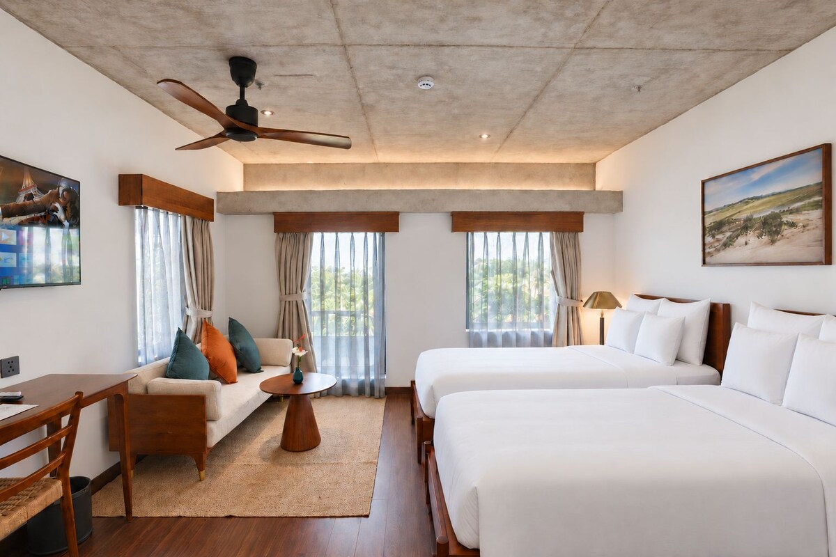 Quarto de hotel com cama, sofá, escrivaninha e ventilador de teto.