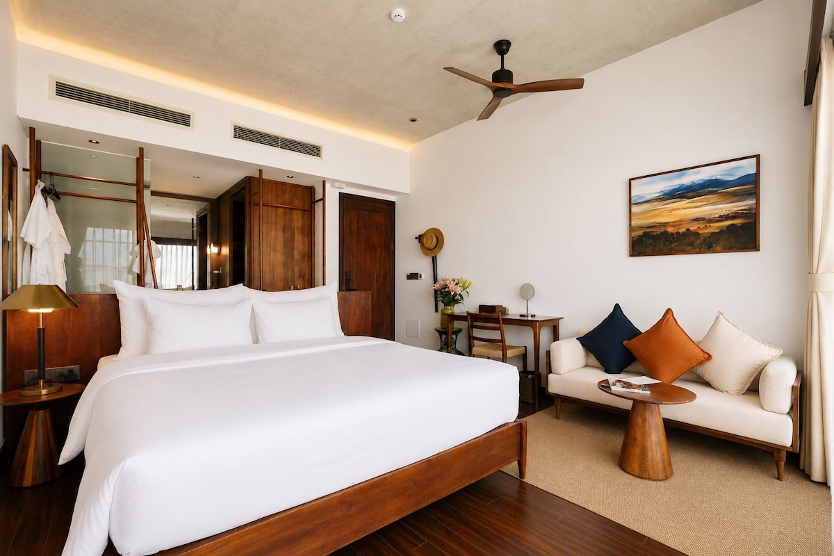 Quarto de hotel com uma cama grande, um sofá, uma mesa pequena e um ventilador de teto.