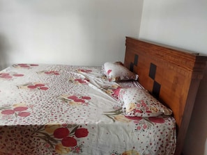 Een bed met bloemenbeddengoed en een houten hoofdeinde in een kamer met effen muren.
