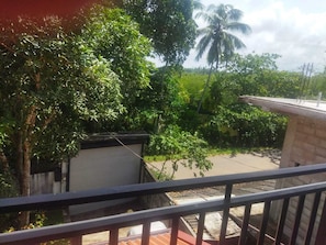 Ein Balkon mit Blick auf eine Straße, Grünflächen und eine Palme.