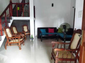 Een woonkamer met een trap, een bank met kleurrijke kussens en twee houten stoelen.