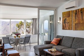 Ein modernes Wohnzimmer mit einer Couch, einem Esstisch mit Stühlen, einem Balkon mit Bergblick und einer Klimaanlage.