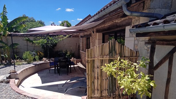 A patio with a table and chairs, a bamboo fence, and a potted plant. - Gite La Granica (restored barn) (Bosset)