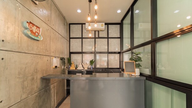 A reception desk with a modern design, a coffee sign, and a large window with a view. - Nawin Hotel Donmueang (Bangkok)