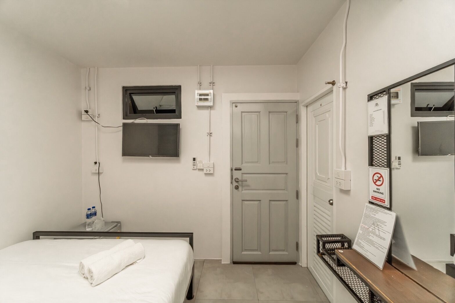 A hotel room with a bed, a television mounted on the wall, a door, and a no-smoking sign.