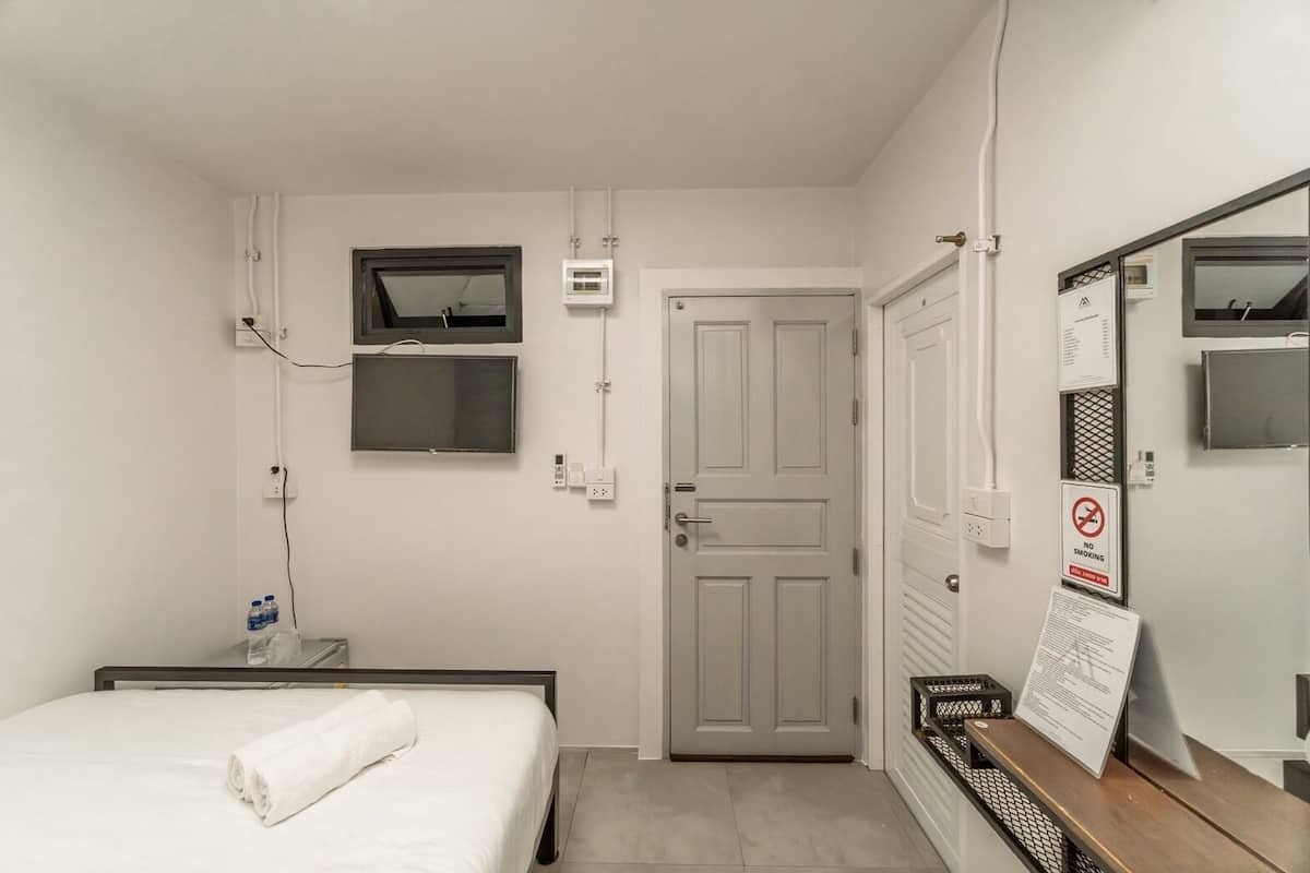 A hotel room with a bed, a television mounted on the wall, a door, and a no-smoking sign.