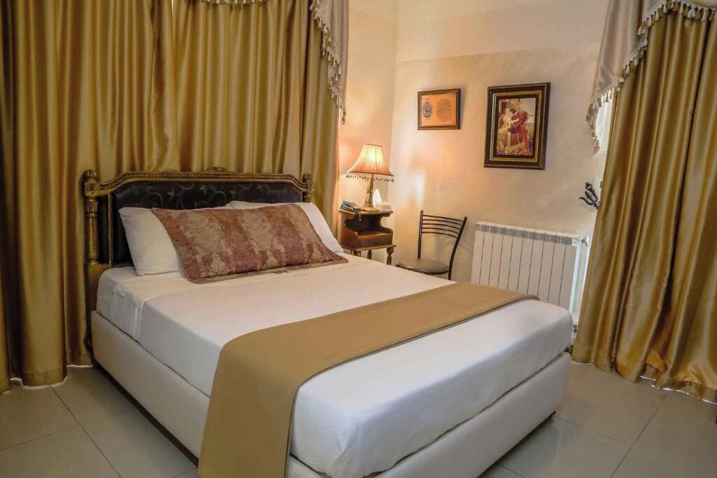 Une chambre d’hôtel avec un grand lit, une table de chevet avec une lampe, une chaise et deux tableaux encadrés au mur.