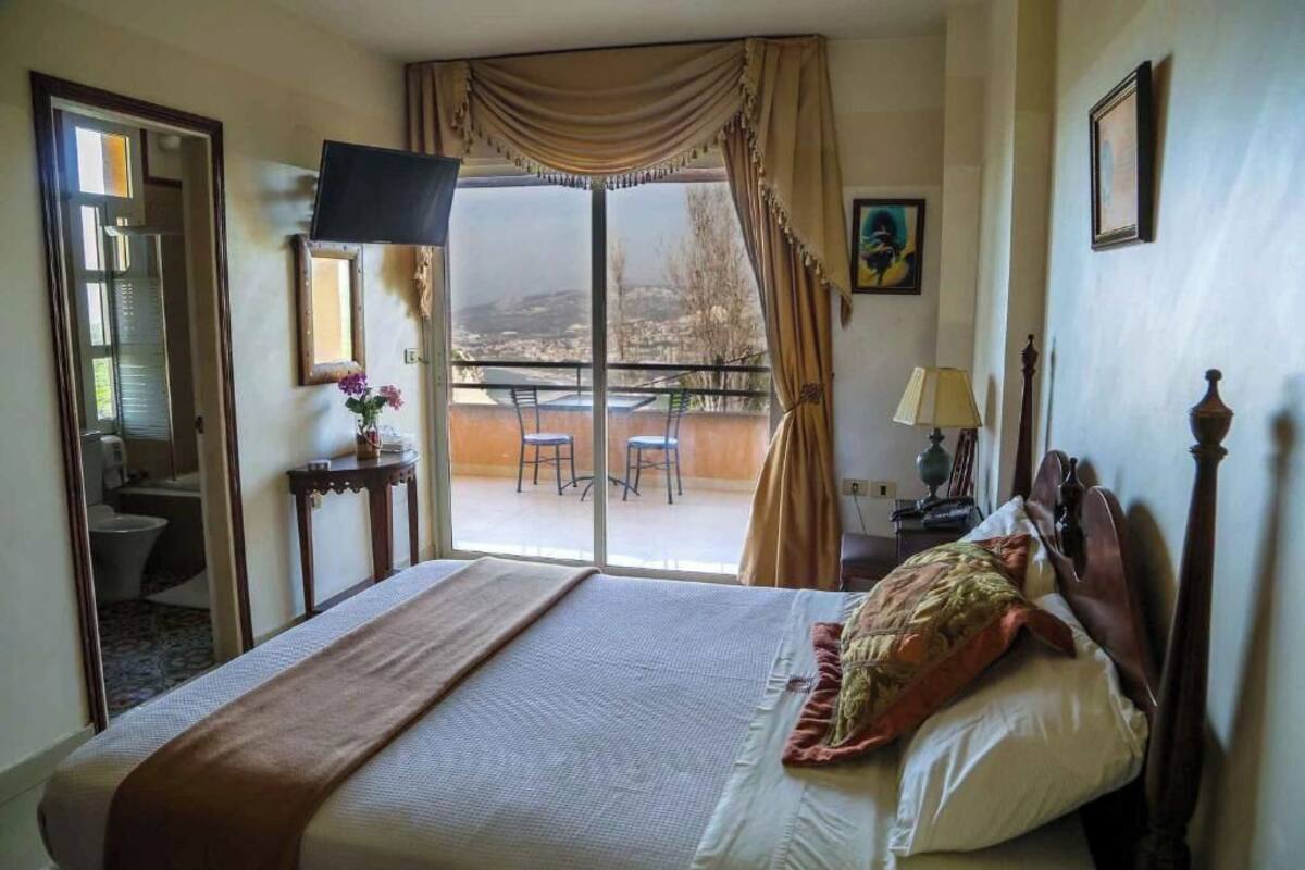 Une chambre d’hôtel avec un lit, une télévision, un balcon avec une table et des chaises, et une vue sur l’extérieur.