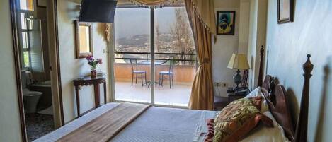 A hotel room with a bed, a TV, a balcony with a table and chairs, and a view of the outside.
