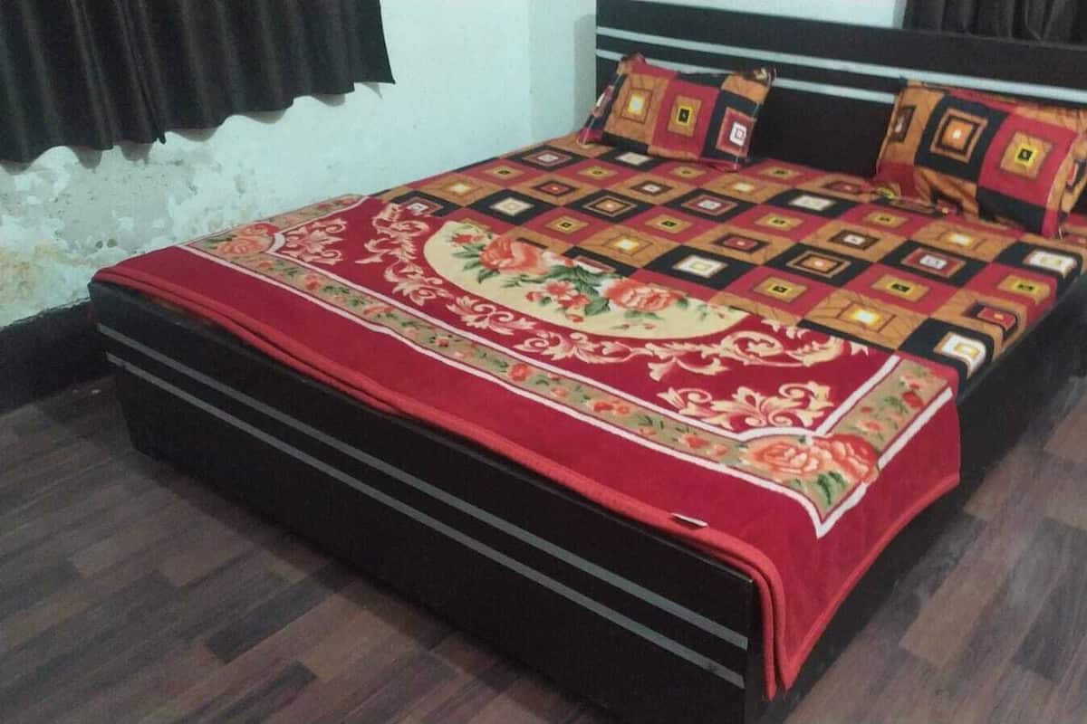 A bed with a floral-patterned bedspread, a dark-colored headboard, and a wooden floor.