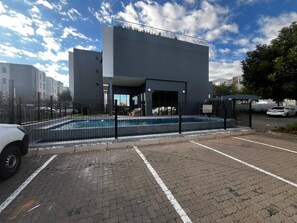 Un bâtiment moderne doté d’une piscine, d’un parking dallé et d’une entrée clôturée.