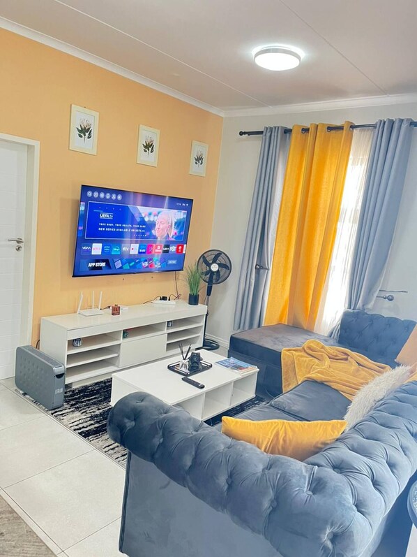 Un salon doté d’un téléviseur à écran plat, d’un meuble de rangement blanc, d’un canapé gris et d’un coussin jaune.