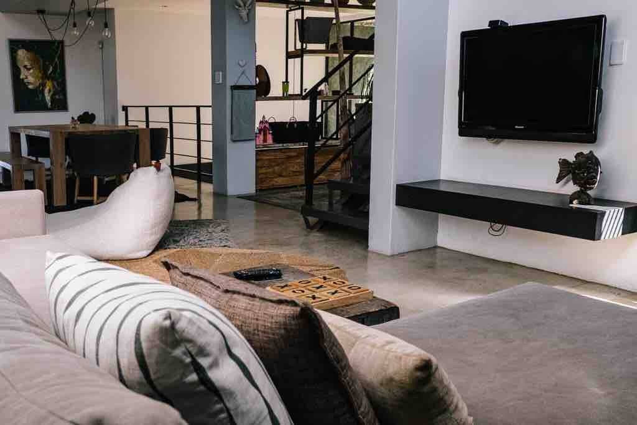 Uma sala de estar moderna com sofá, mesa de centro, televisão de tela plana na parede e escada que leva a um andar superior.