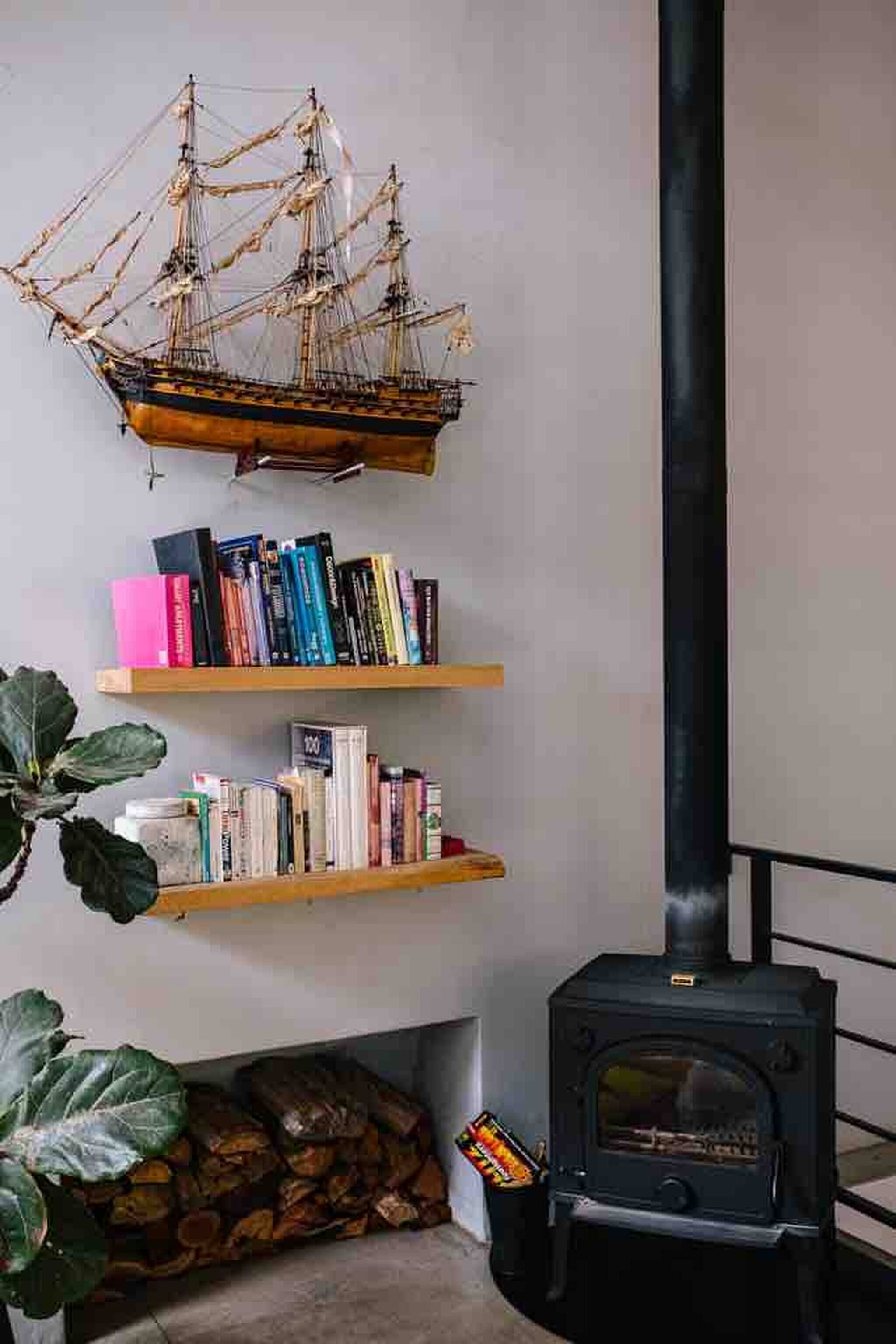 Een kamer met een houten boekenkast, een model schip, een open haard en een grote plant.